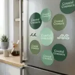 Round coastal coaster branded magnets in dark green, sage, and mint shades displayed on a stainless-steel refrigerator.